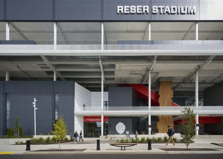 Modern stadium exterior with sleek architecture and people walking by. Captured on a clear day for a vibrant urban scene.