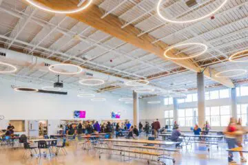 Modern cafeteria with open seating, contemporary lighting, and people dining and socializing in a spacious, well-lit environment.