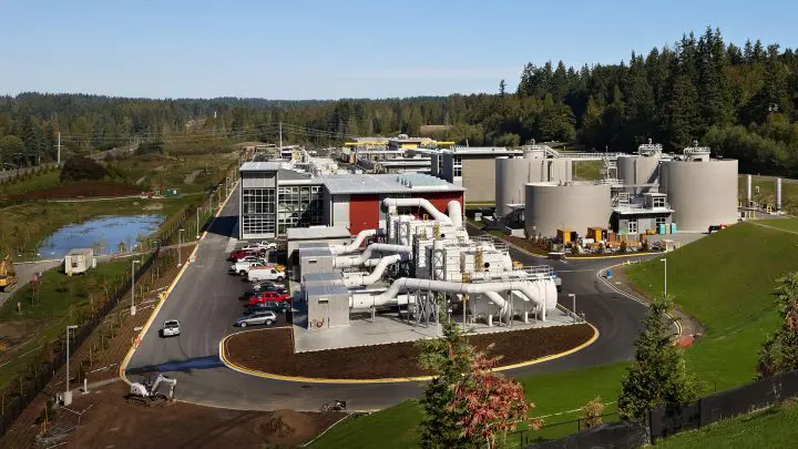 Aerial view of a modern wastewater treatment plant surrounded by lush greenery and vibrant blue skies.