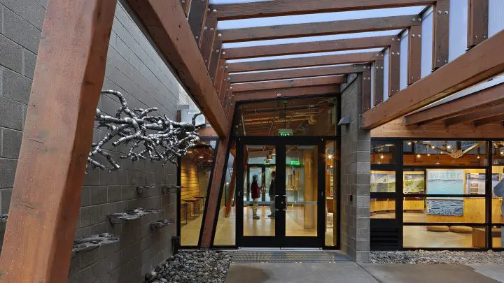 Modern architectural entrance with glass doors and metal art, featuring a sleek wood and stone design.