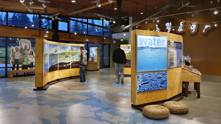 Modern exhibit space with interactive water-themed displays, welcoming environment, visitors engaging, educational atmosphere.