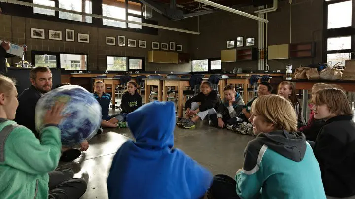 Teacher and students sit in a classroom circle with a globe, engaging in a fun, interactive learning session.