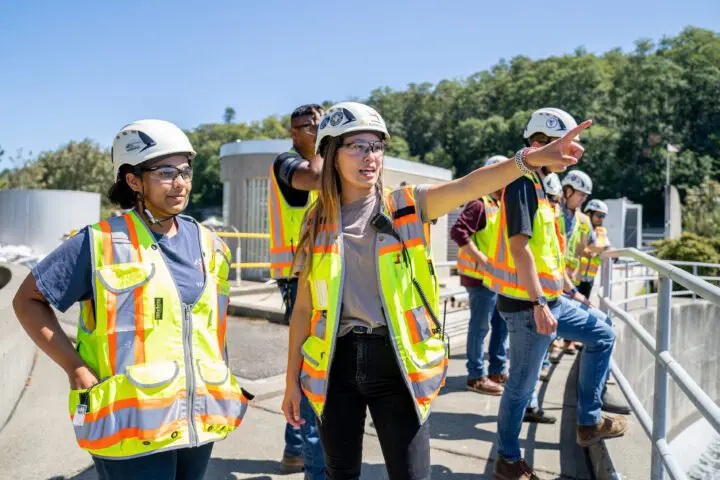 Construction team in hard hats and safety vests observing a site, with one individual pointing and directing focus.
