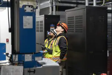 Workers wearing safety gear inspecting machinery in an industrial setting.