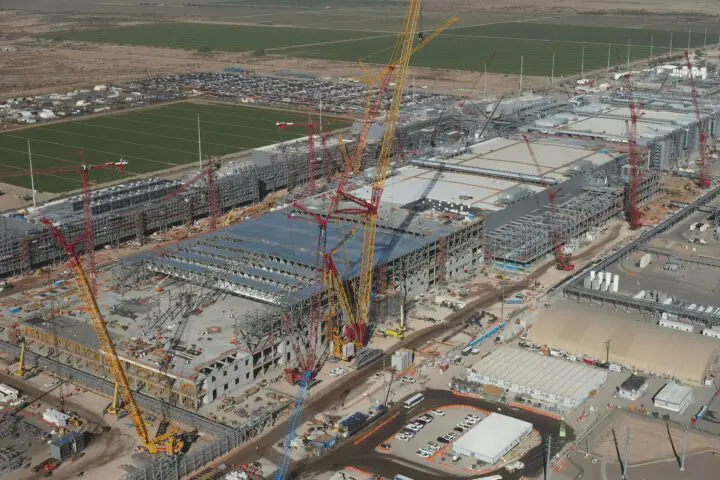 Aerial view of a large construction site with cranes and partially built structures in a desert setting.