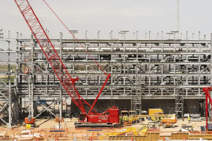 Construction site with red crane and workers assembling a steel structure against a clear sky background.