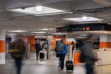 People with luggage walking in an airport parking garage, following signs for transportation options. Bright and busy setting.
