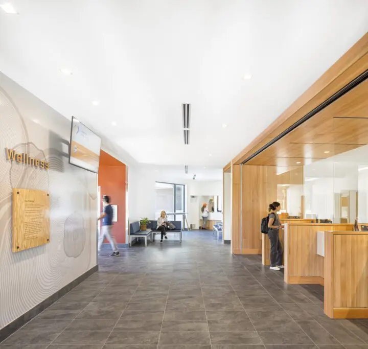 Modern wellness center lobby with wooden reception, seating area, and people interacting. Bright, spacious, and inviting atmosphere.