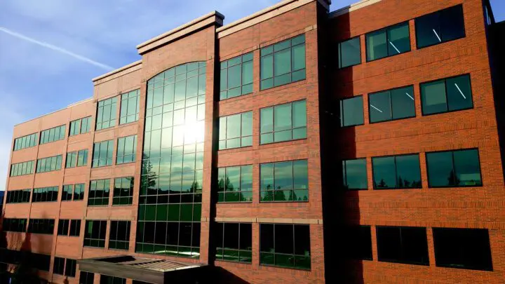Modern brick office building with sun reflecting on large windows under a clear blue sky.