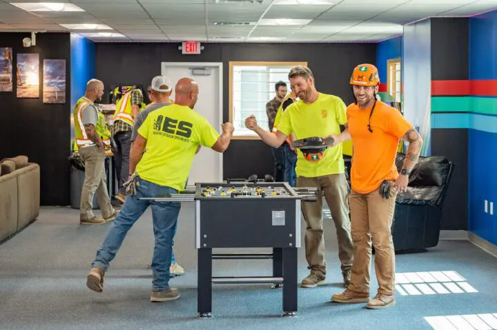 Construction workers enjoying a game of foosball during a break, showcasing teamwork and camaraderie in a vibrant office space.