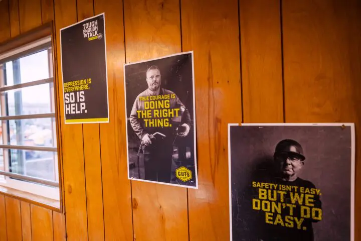 Wood-paneled wall with motivational posters about mental health, courage, and safety for workplace well-being.